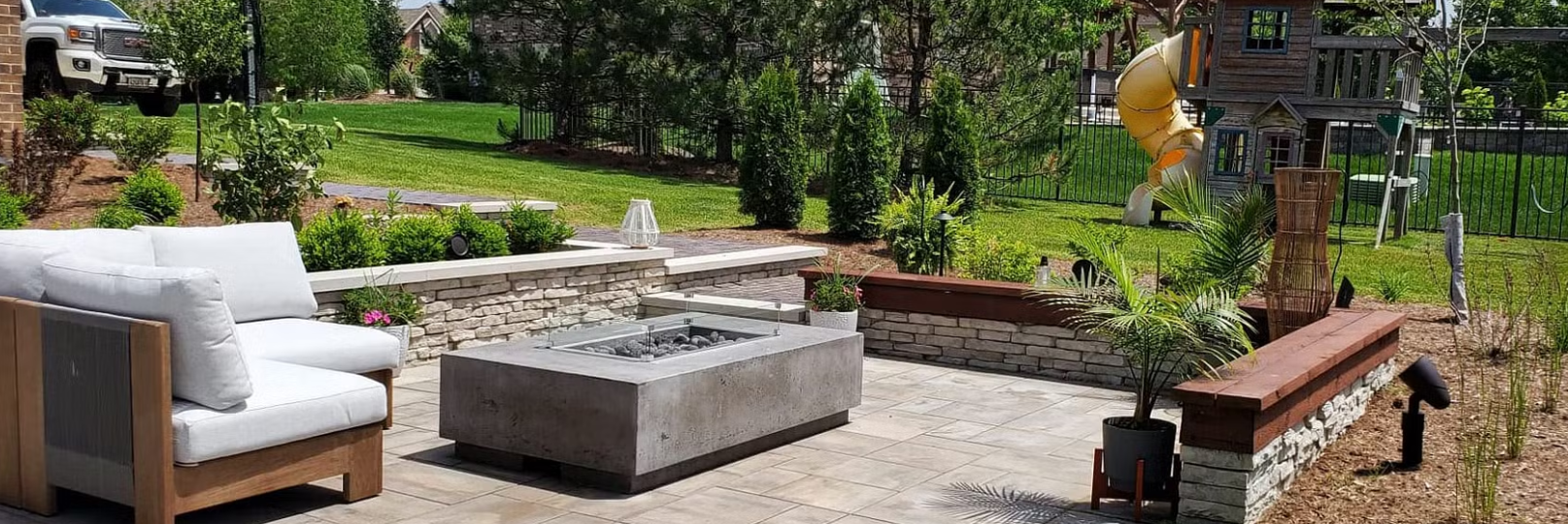 Outdoor patio with a fire pit, seating area, and lush landscaping in a backyard.