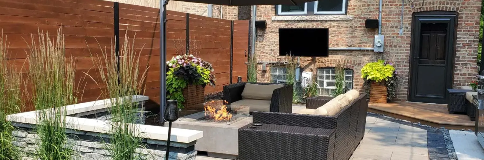Outdoor patio with seating, a fire pit, a TV, and a wooden fence.