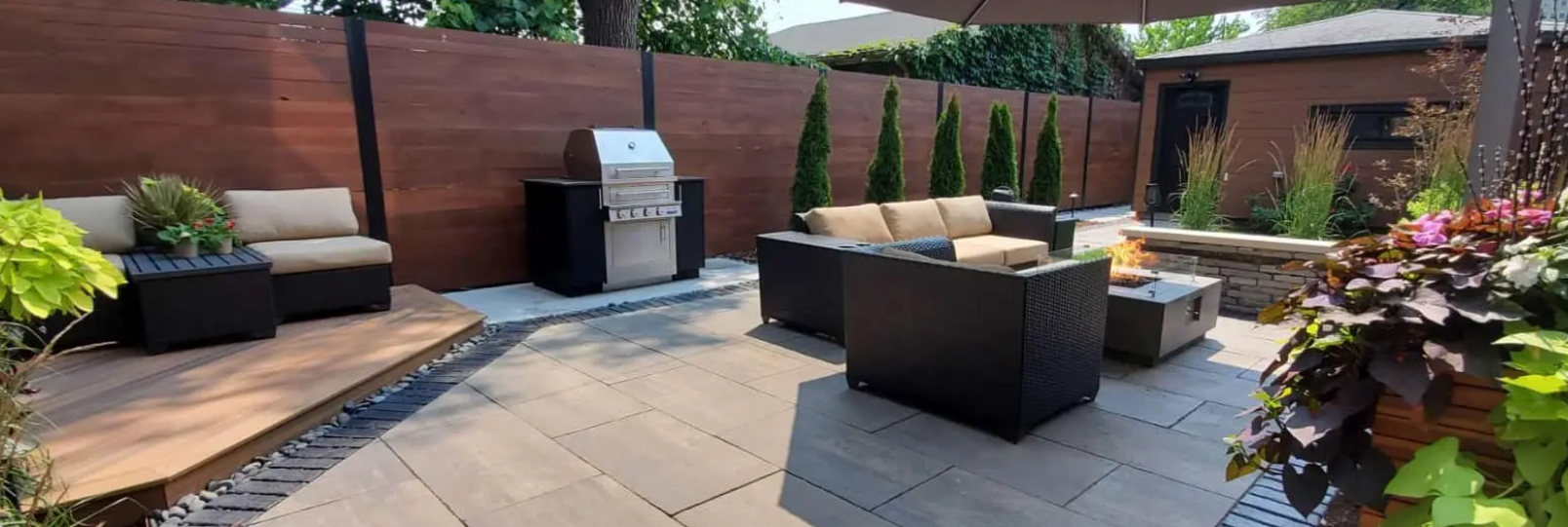 Patio with dark brown wicker furniture, grill, and wooden fence.