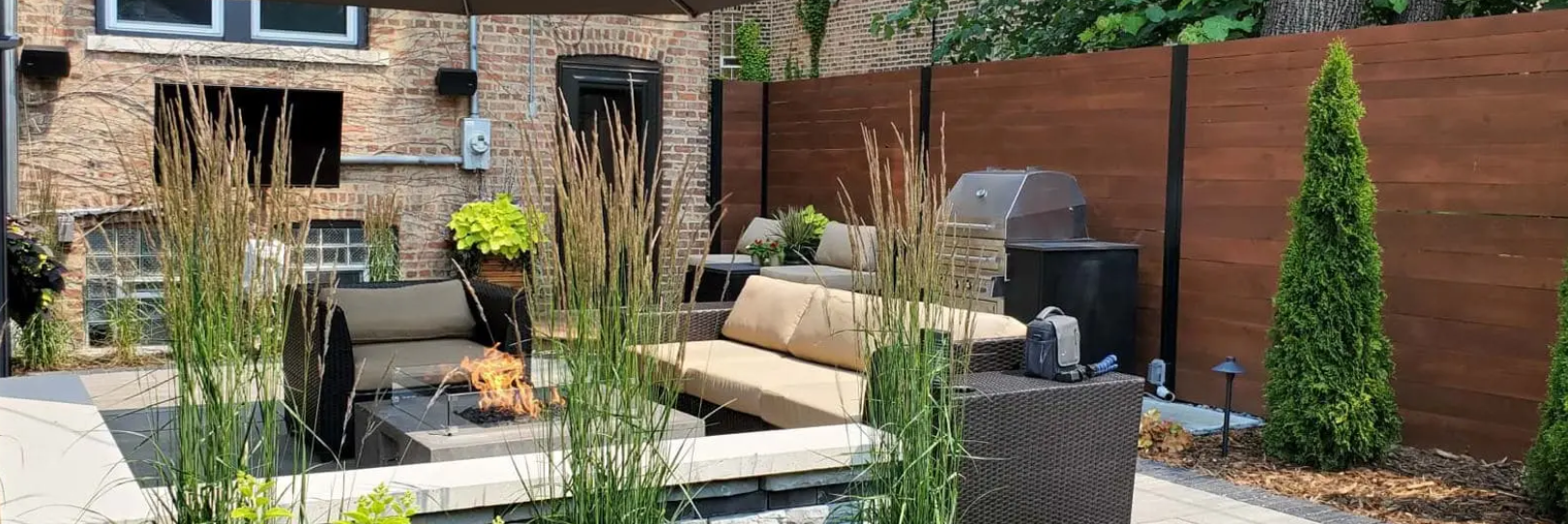 Outdoor patio with seating, a grill, and a brick wall with a wooden fence.