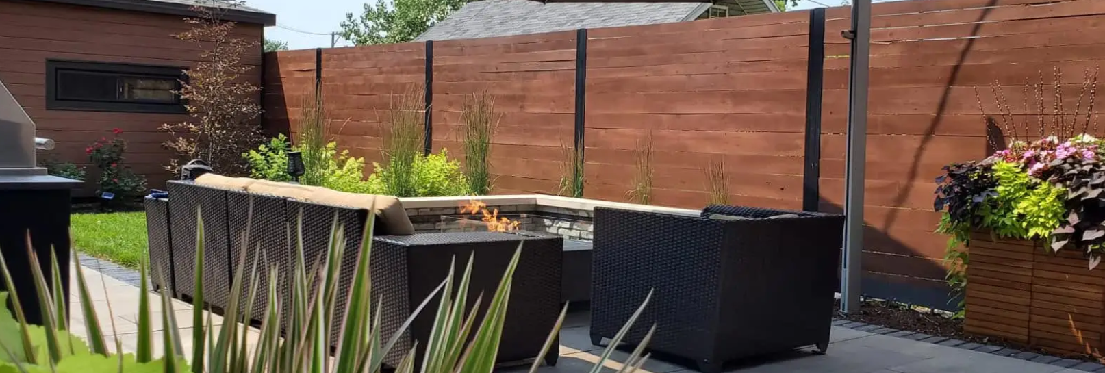 Outdoor patio with a fire pit and seating, enclosed by a wood fence and plants.