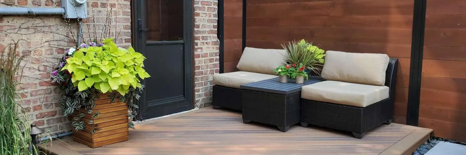 Outdoor seating area with sofa and coffee table on a wooden deck. Bright green plant in a basket.