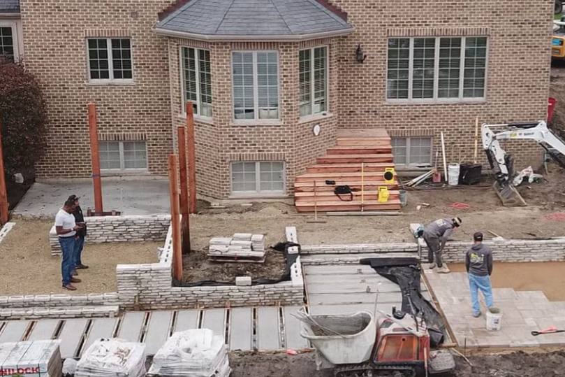Construction site with workers, brick house, retaining walls, and materials.