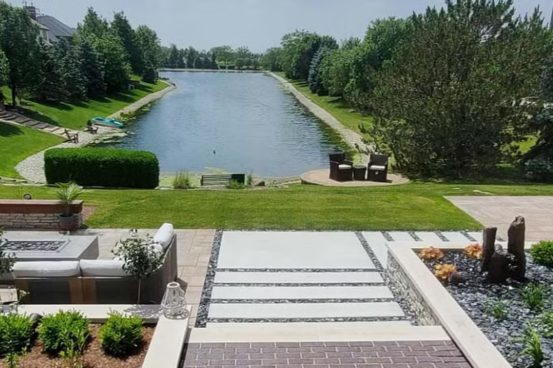 Patio overlooking a lake with lawn and seating areas.