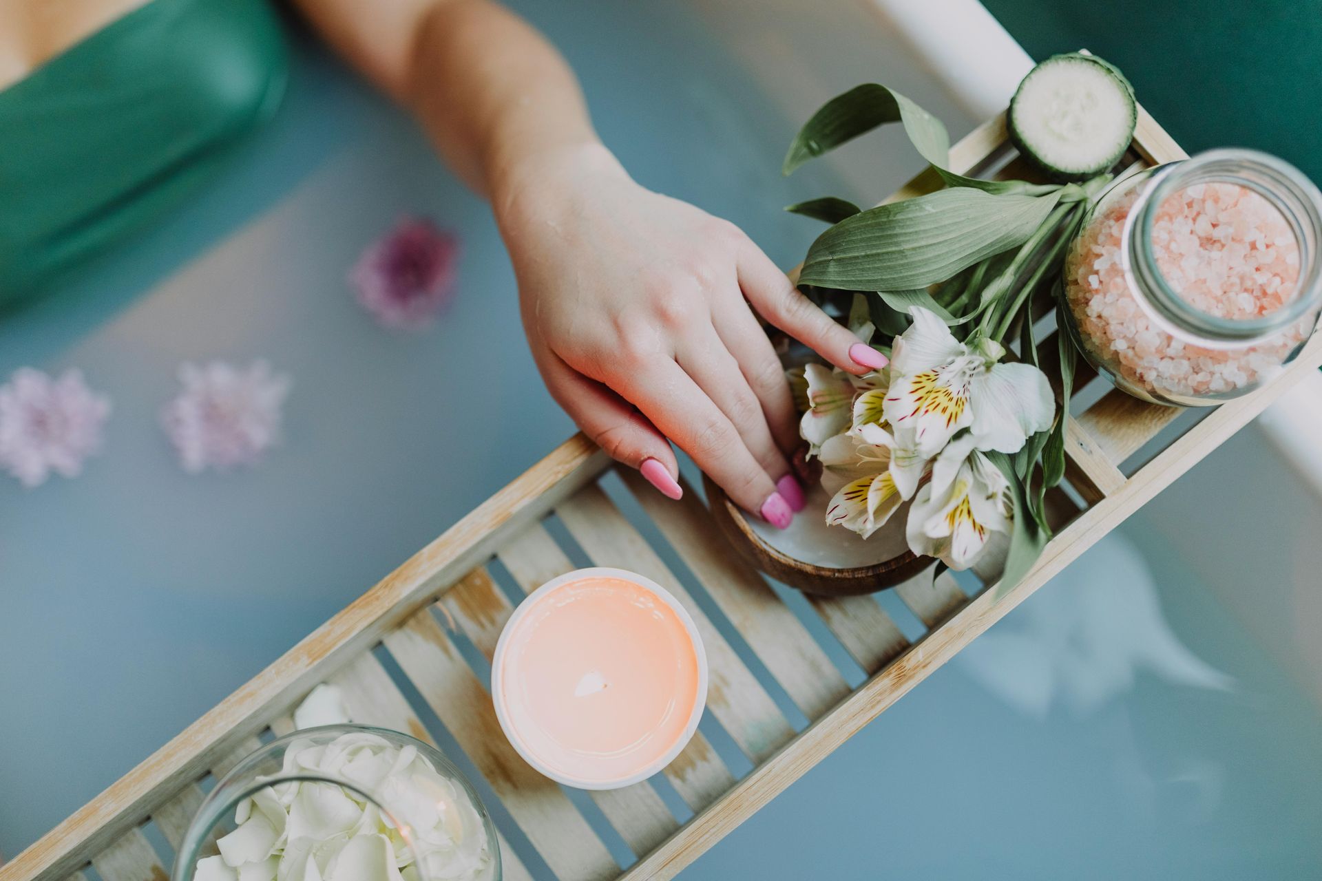 A woman is taking a bath with flowers and candles on a wooden tray.