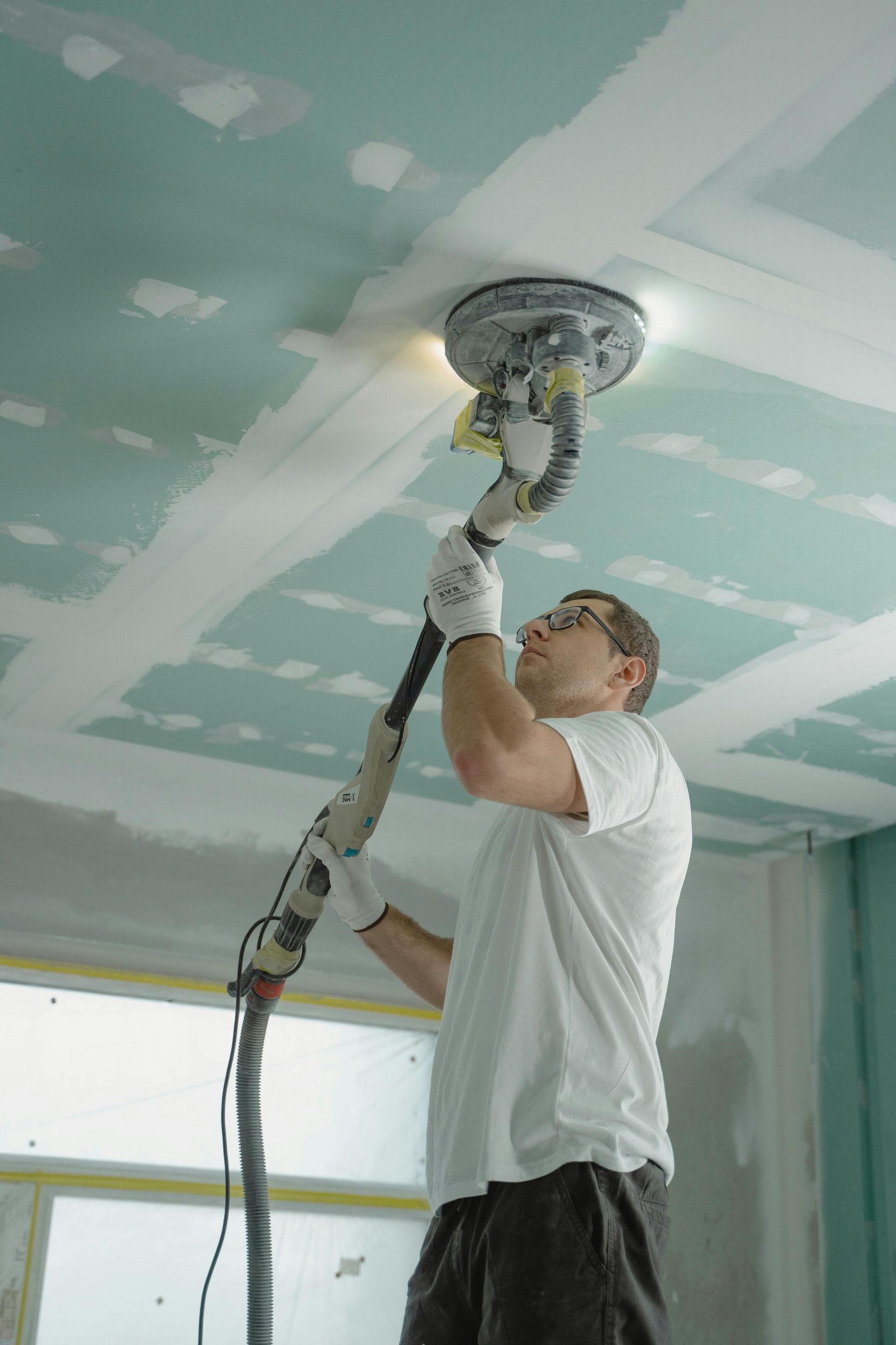 Worker sanding a ceiling with a pole sander in a room under renovation
