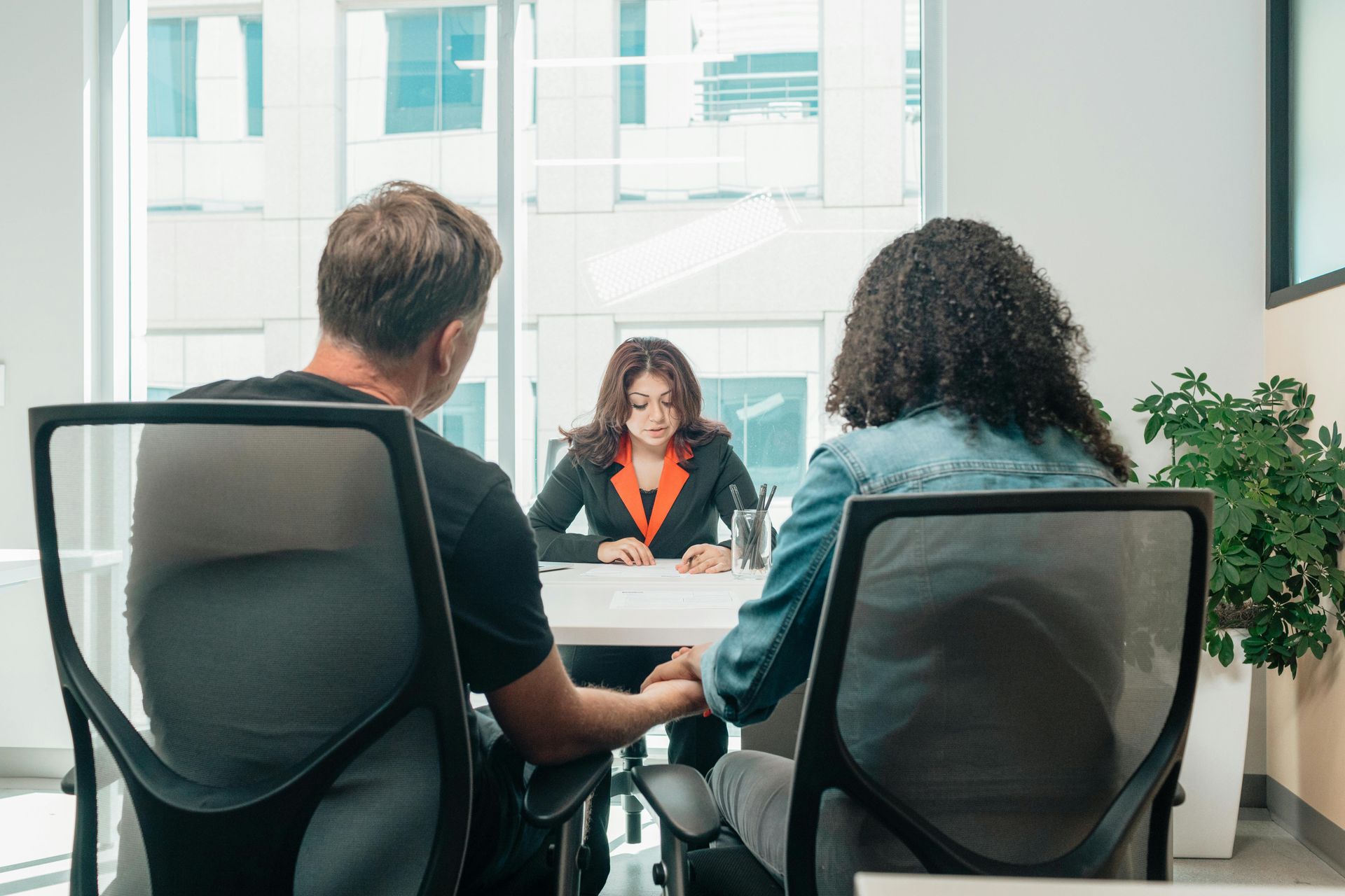 Couple consults with a person at a table in a modern office. They are seated, looking at paperwork.