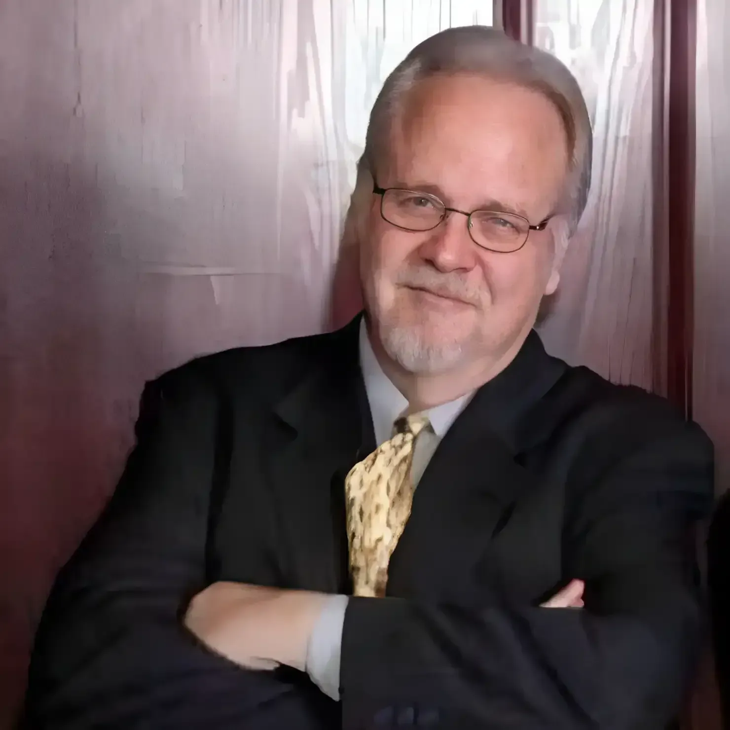 Man with glasses in suit, arms crossed, smiling slightly.