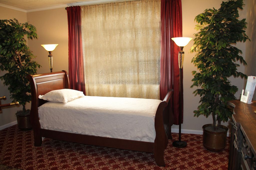 A bedroom with a bed, red carpet, and two floor lamps with faux plants on either side.