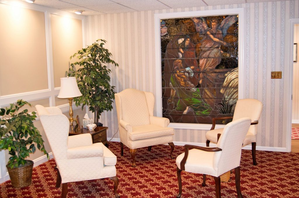 Four cream-colored chairs in a room with a large stained glass window. Red and white patterned carpet.