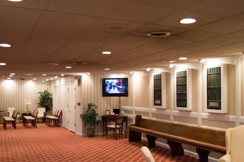 A room with chairs, benches, and a TV, likely a waiting area in a funeral home.