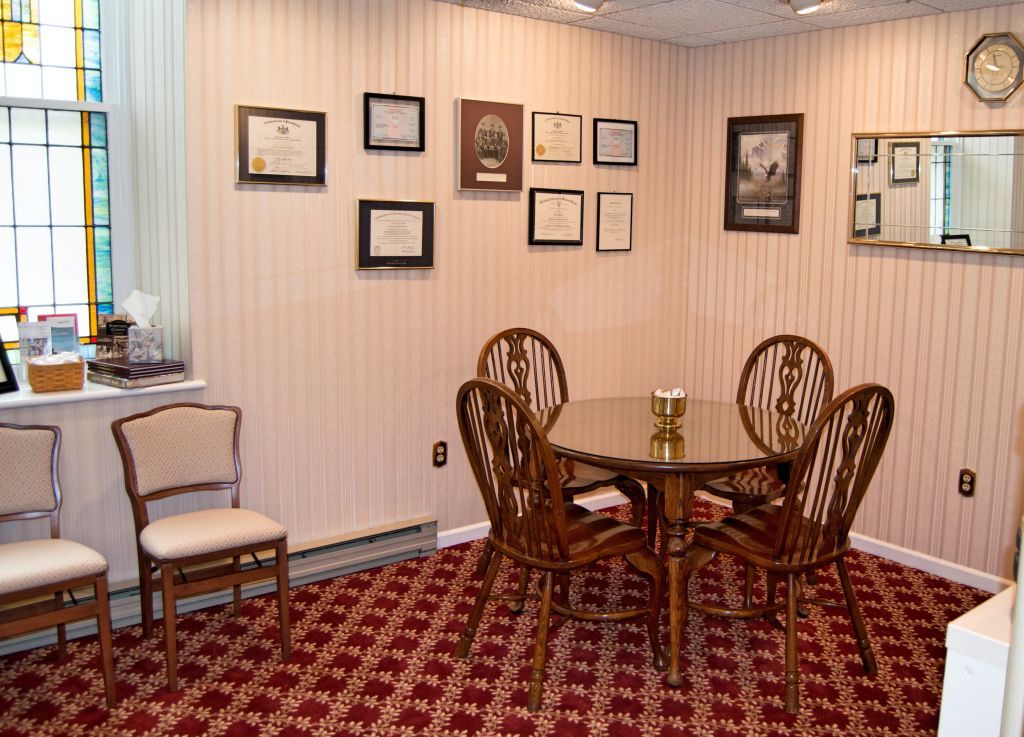 A small, carpeted waiting room with a table and chairs, decorated with framed certificates.
