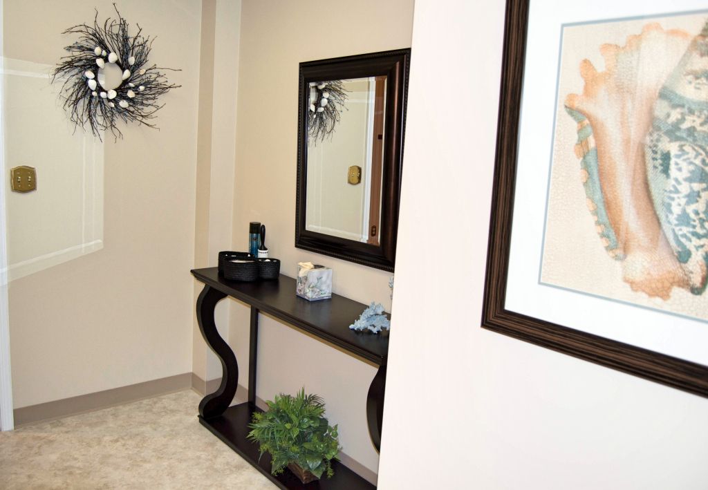 Hallway with console table, mirror, and artwork; neutral walls and carpet; decorative wreath.
