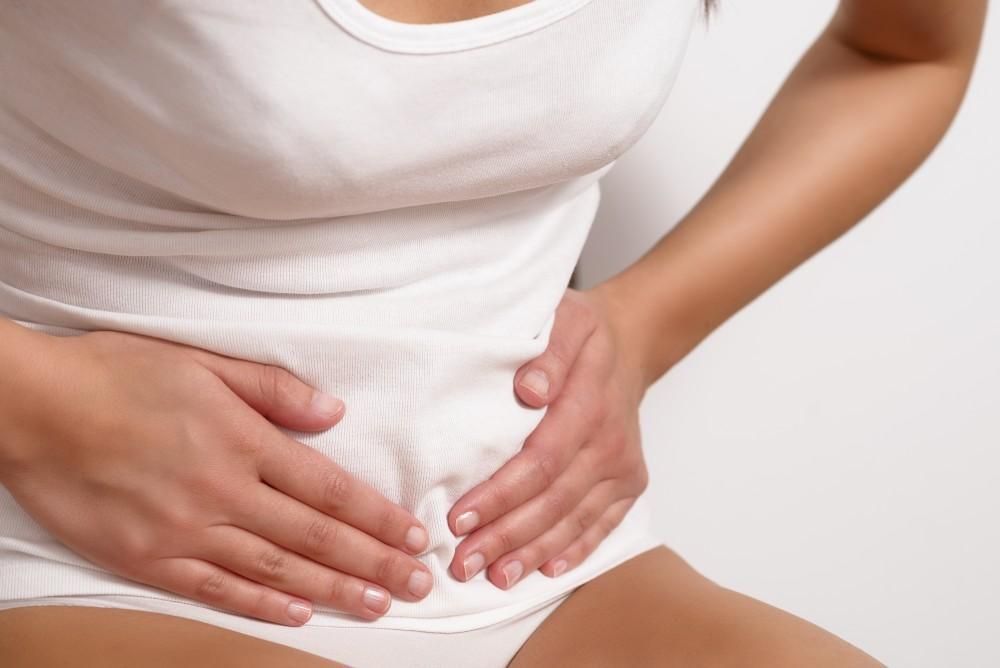 Woman in white clothing holding lower abdomen, representing discomfort related to fecal incontinence