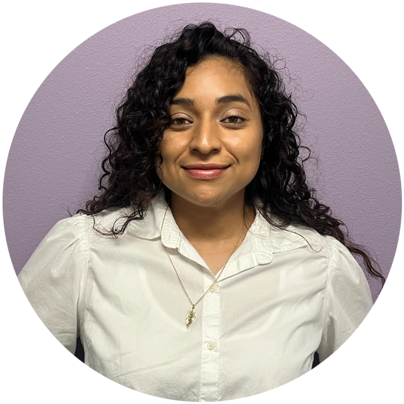 Woman with curly hair wearing a white collared shirt, smiling, against a purple background.