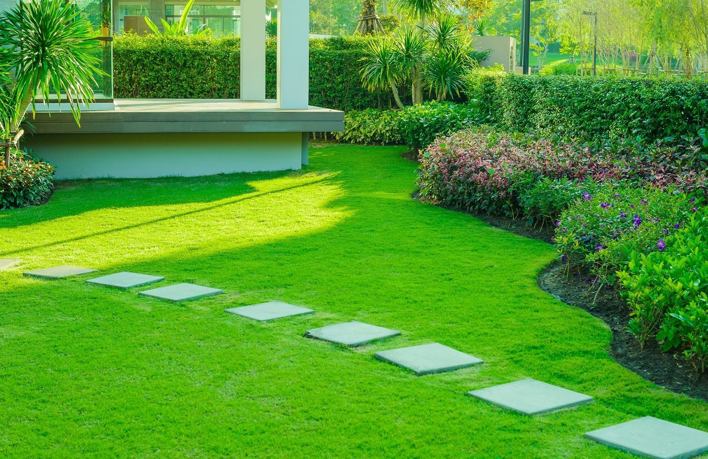 Green lawn with stepping stones leading to a gazebo, surrounded by manicured shrubs and flowerbeds.