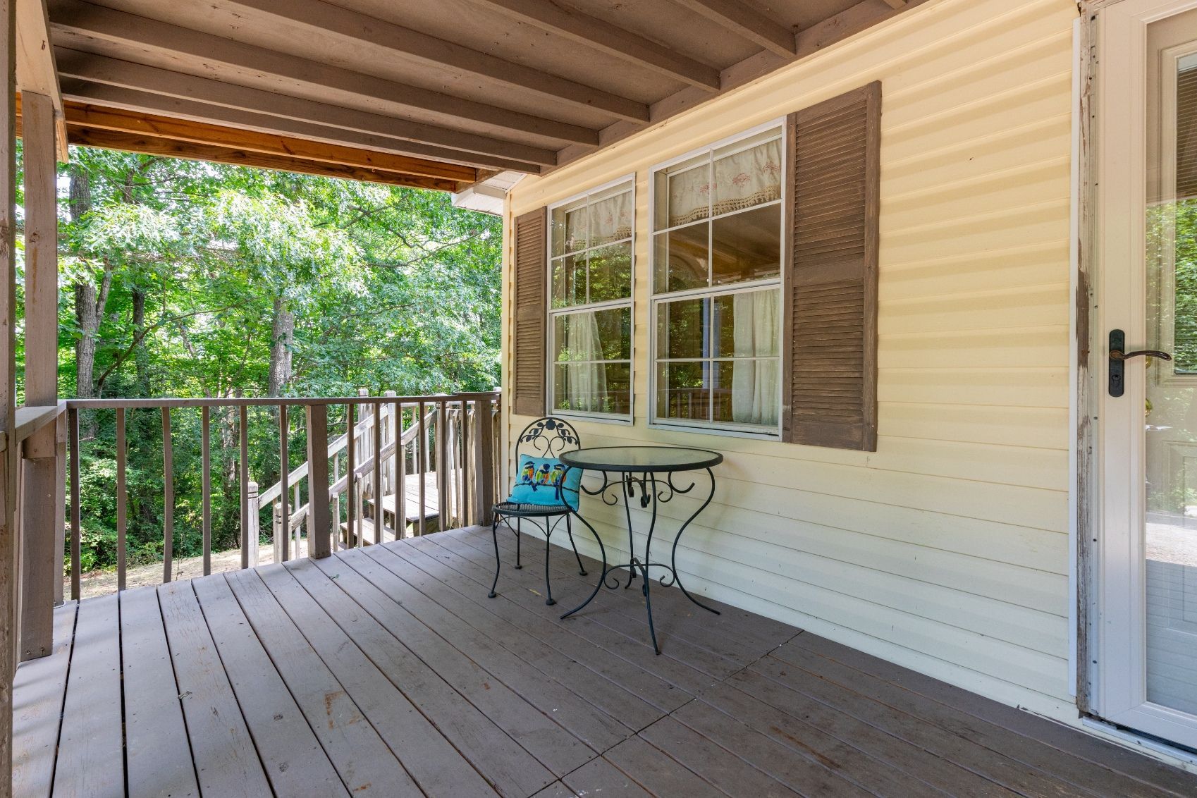 Porch with table, chair, and window with open shutters. Overlooking trees and foliage.