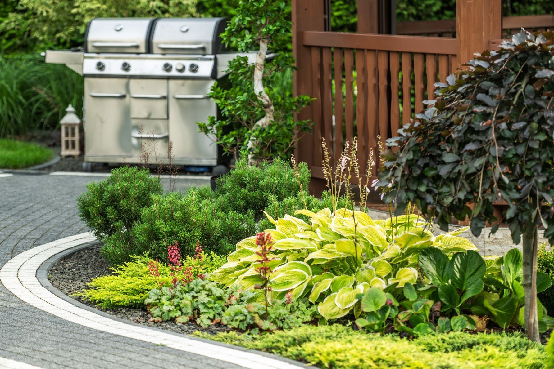 Outdoor barbecue grill next to a landscaped garden and a wooden gazebo.