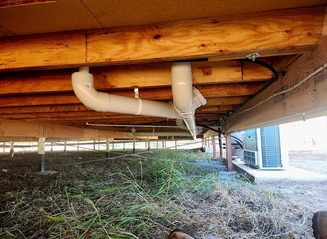 Person in blue gloves assembles plumbing under a sink with white tile.