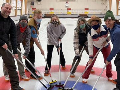 A group of people are standing on a curling rink holding brooms.