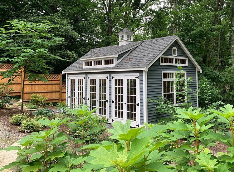 A small house with a lot of windows and doors is surrounded by trees.