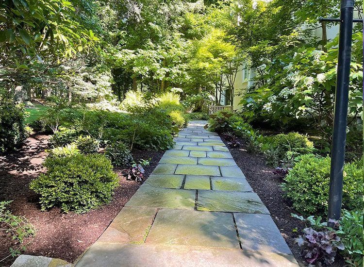 A stone walkway in a garden surrounded by trees and bushes.
