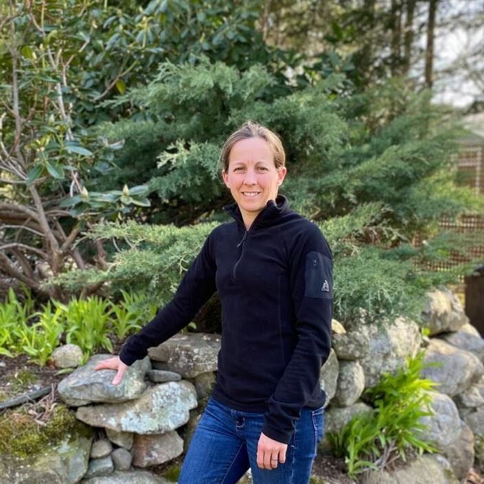 A woman in a black sweater is standing next to a stone wall.