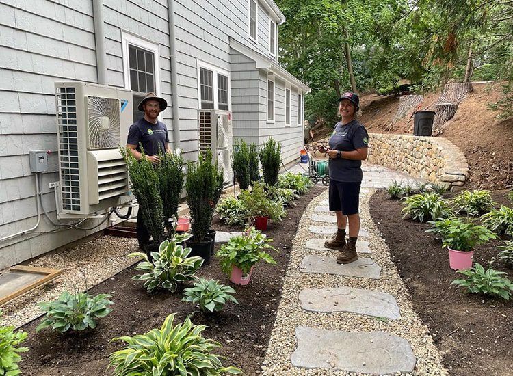 Two men are standing next to each other in a garden next to a house.