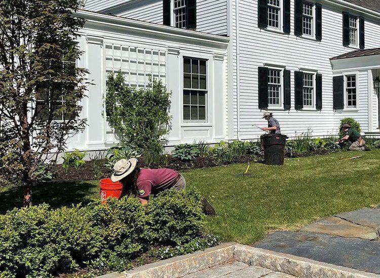 A man is kneeling in the grass in front of a white house.