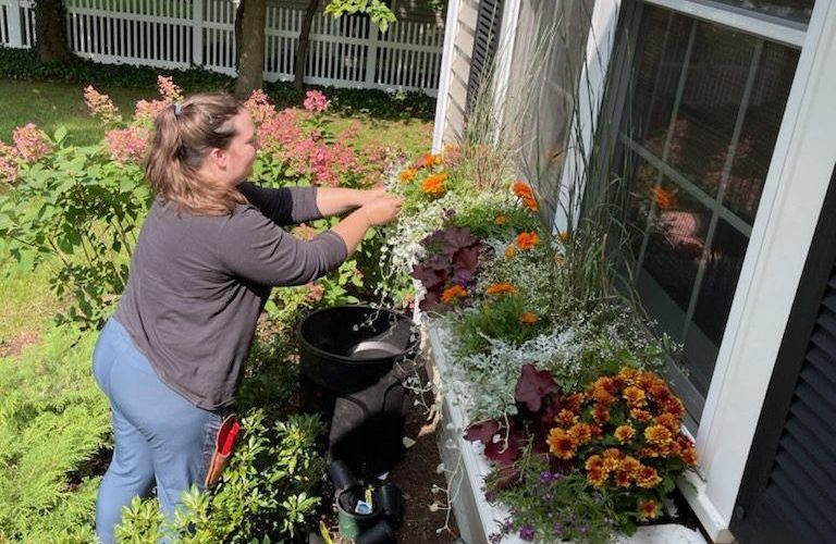 A woman is planting flowers in a window box.