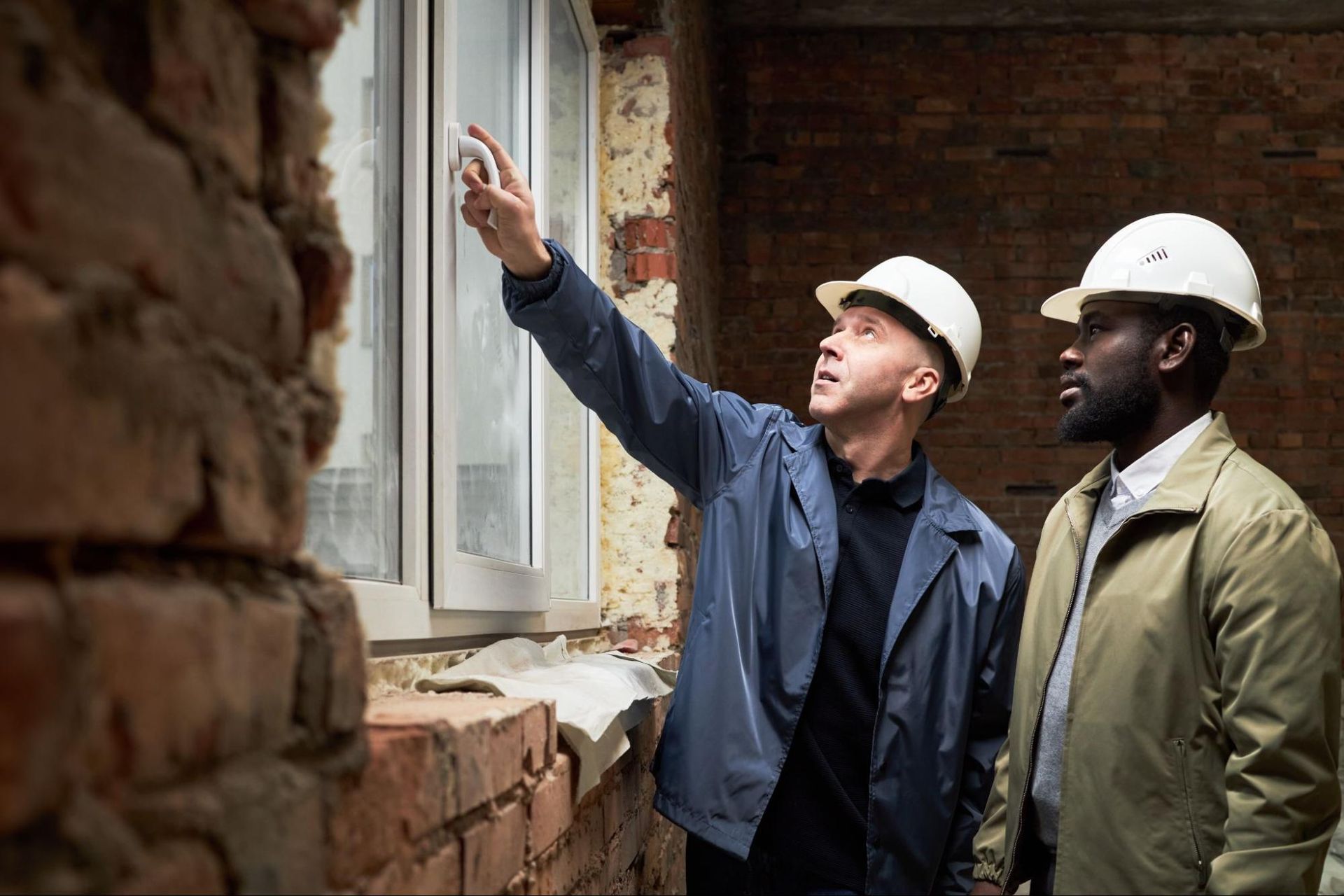 two men in hard hats looking at window