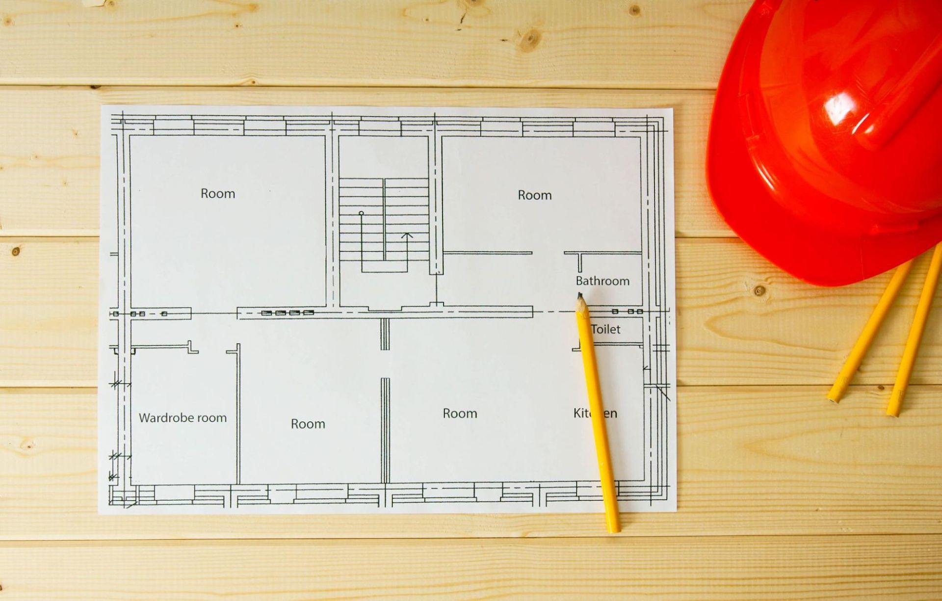 Architectural floor plan with red hard hat and yellow pencil symbolizing property evaluation and building inspection process.