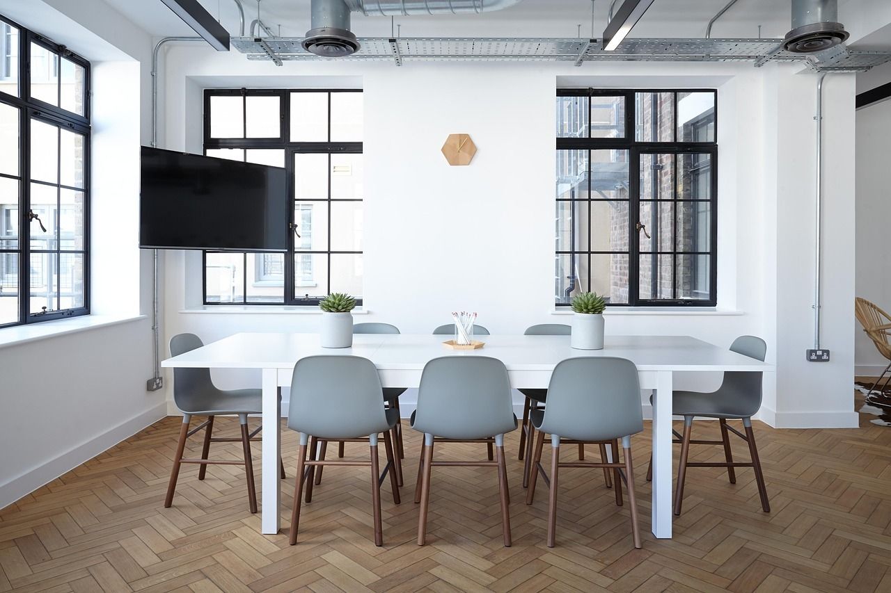 Modern conference room with white table, gray chairs, and large black-framed windows.
