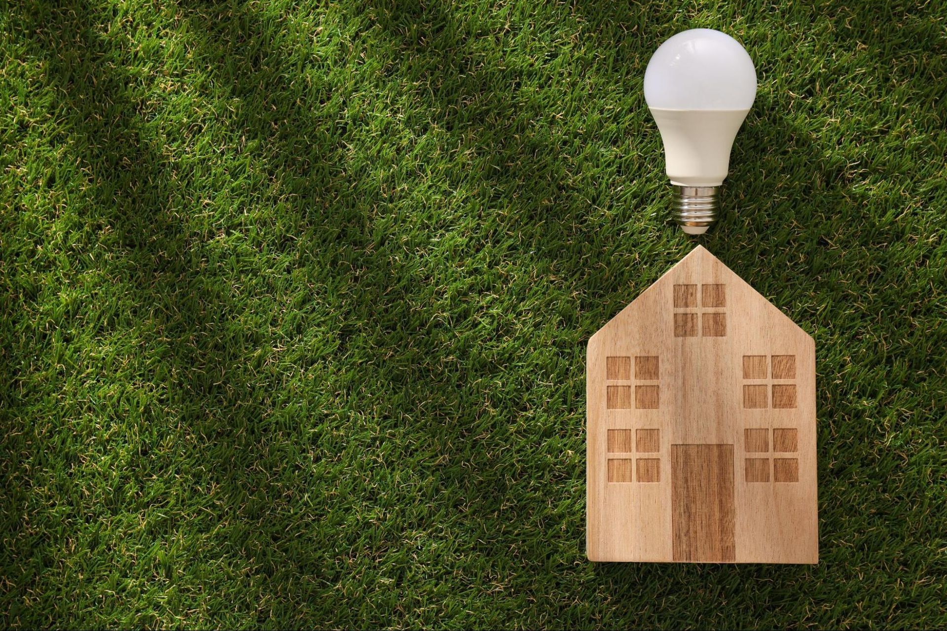 miniature house with lightbulb on grass, representing high electric bill home energy inspection
