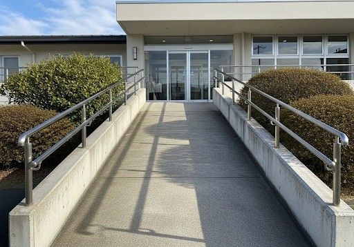 A gently sloped concrete wheelchair-accessible ramp with handrails leading up to a building entrance
