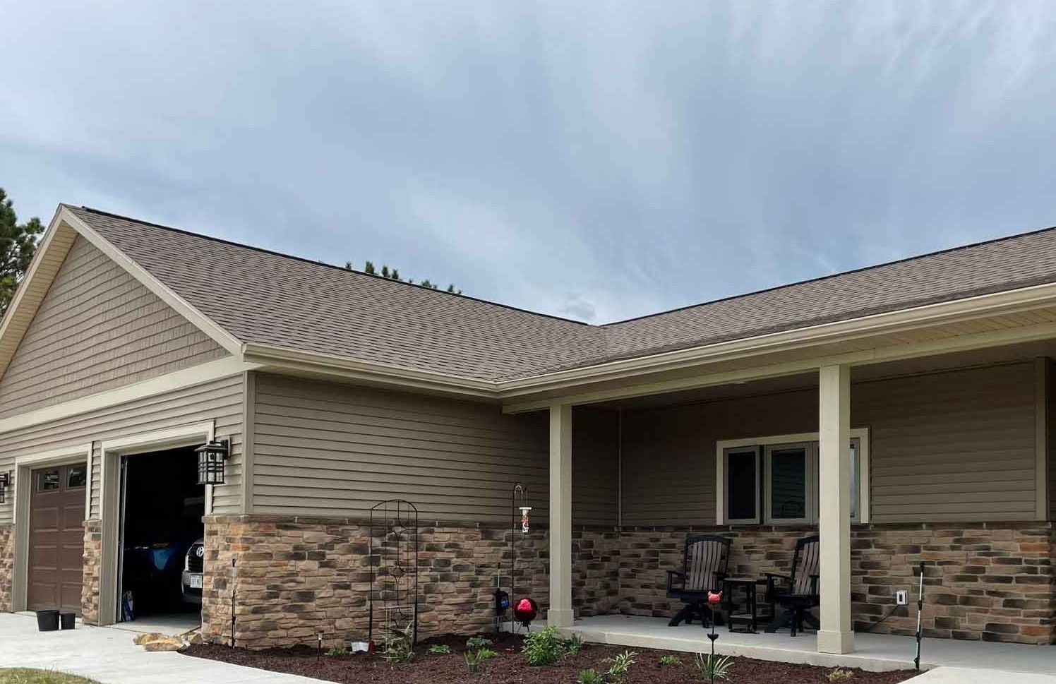 Tan house with brown brick, garage, and porch; cloudy sky overhead.