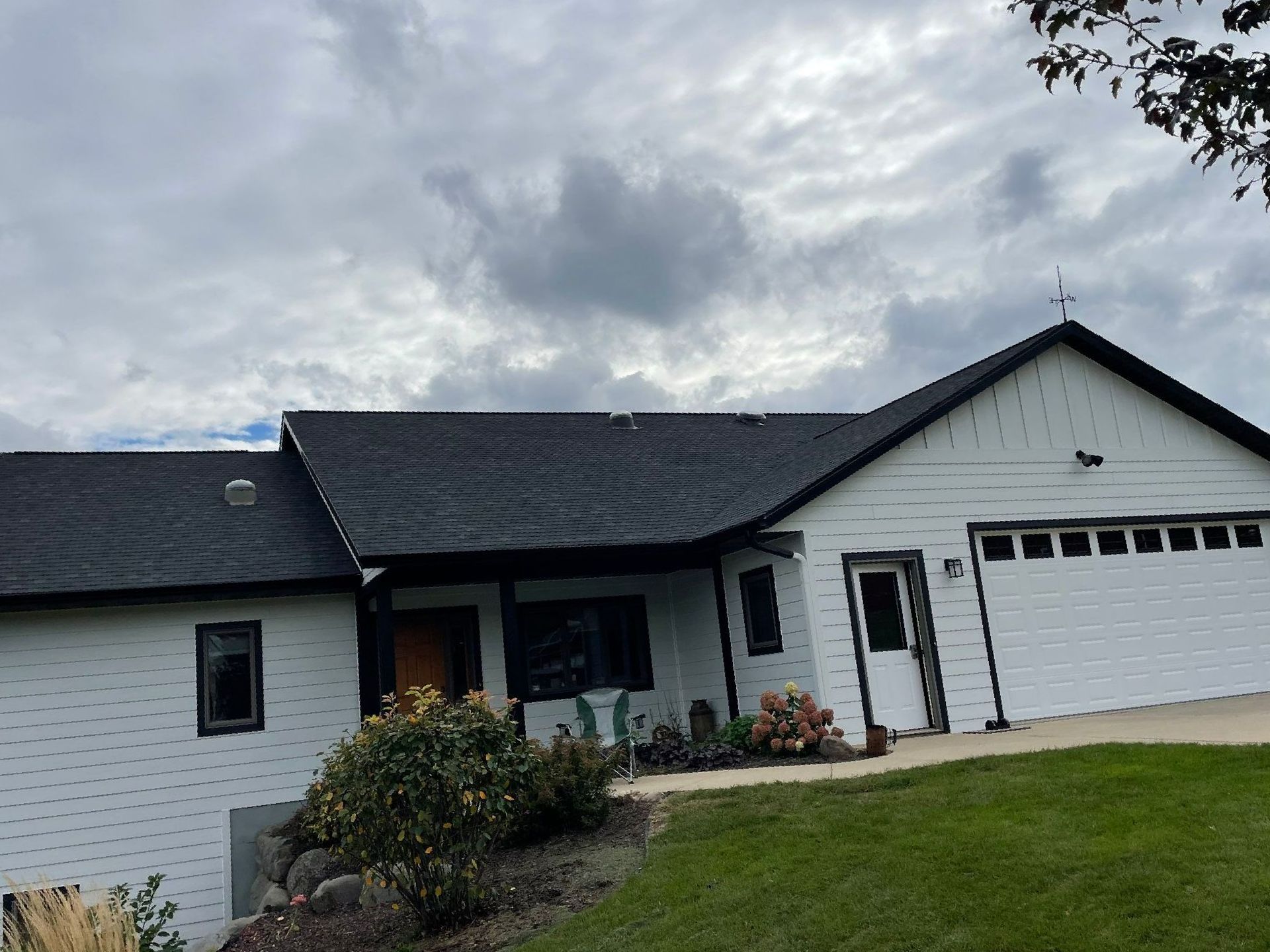 White house with black roof and trim, cloudy sky, green lawn.