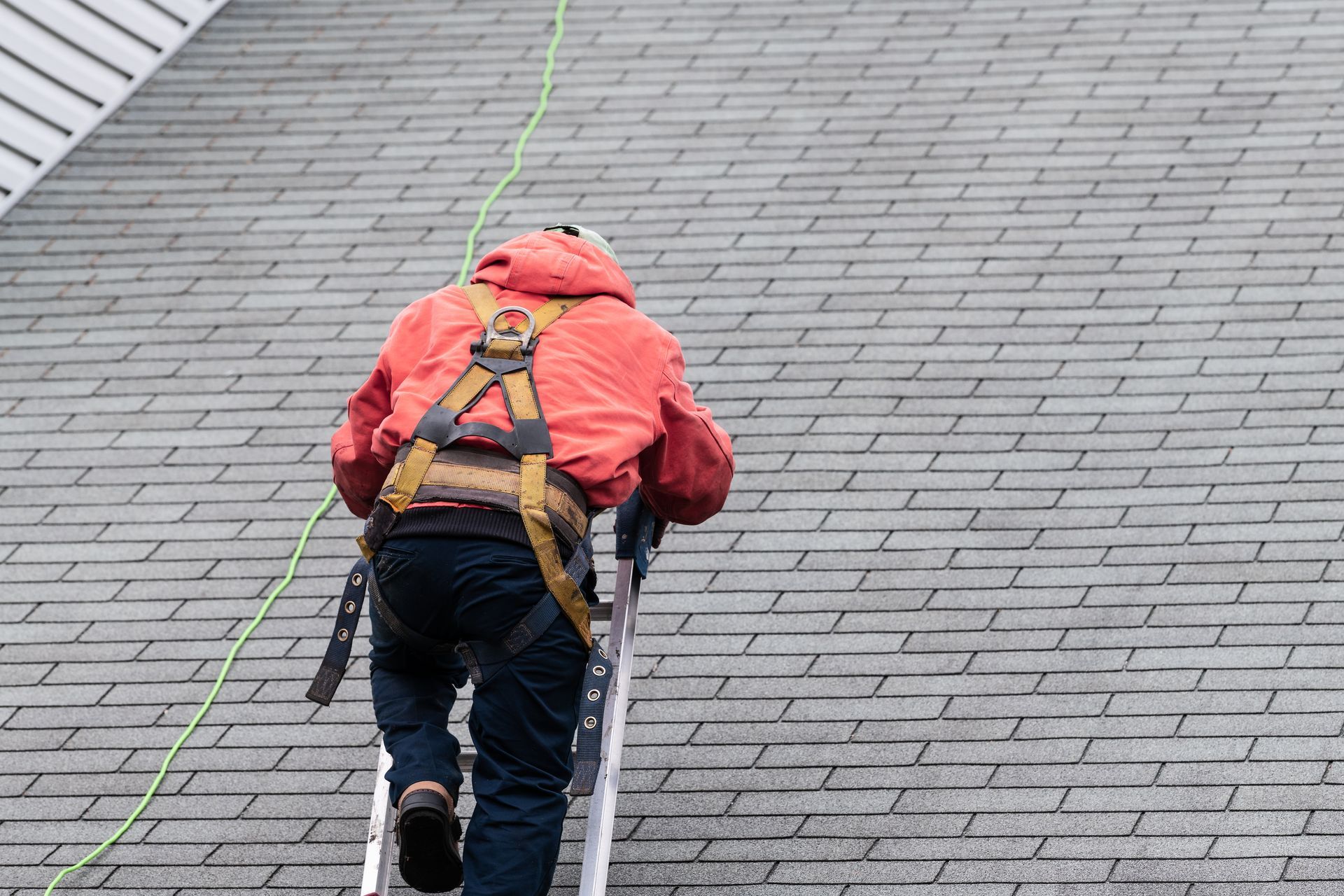 A roofer climbing a ladder onto a shingle roof.