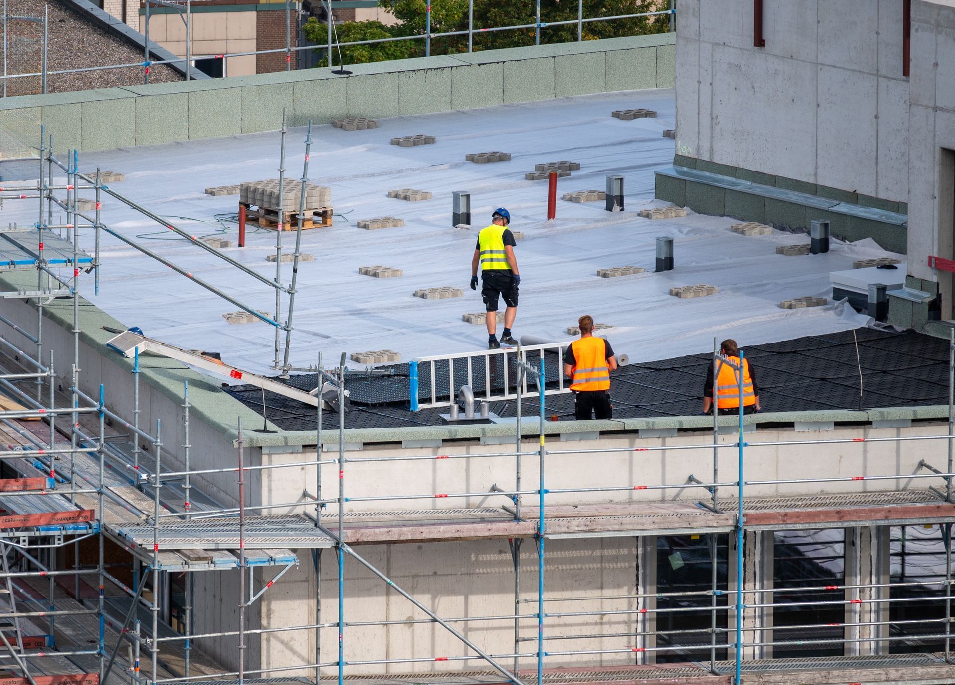 Bird’s-eye view of a roofer waterproofing the flat roof of a commercial building. 