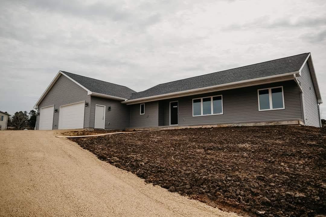 Gray house under construction on a slight hill with a gravel driveway. Cloudy sky.