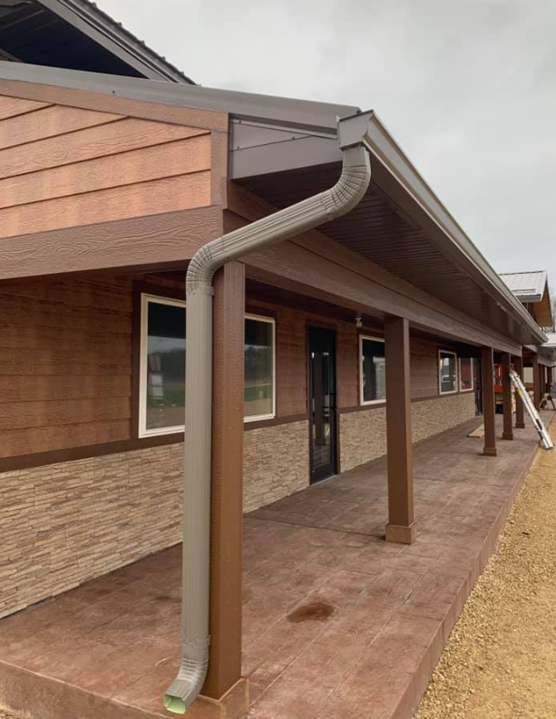 Brown building with a covered porch, gutters, and windows.