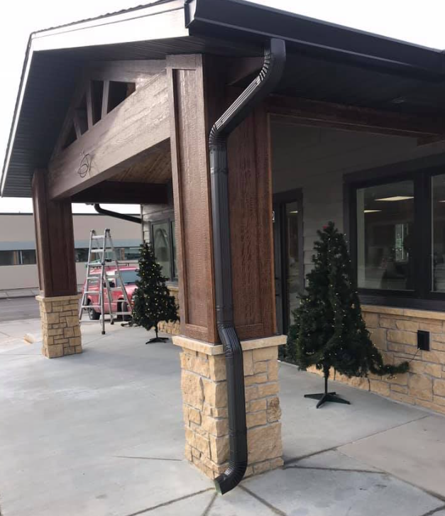 Brown and tan building exterior with black gutters and small Christmas trees.