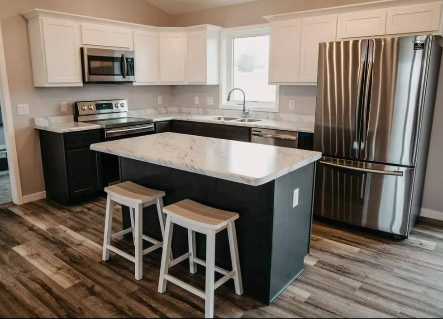 Modern kitchen with white upper cabinets, black lower cabinets, island with stools, and stainless steel appliances.