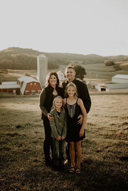 A family is posing for a picture in a field with a barn in the background.