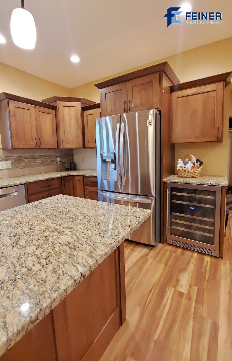 Kitchen with wooden cabinets, granite countertops, stainless steel fridge, and wine cooler.