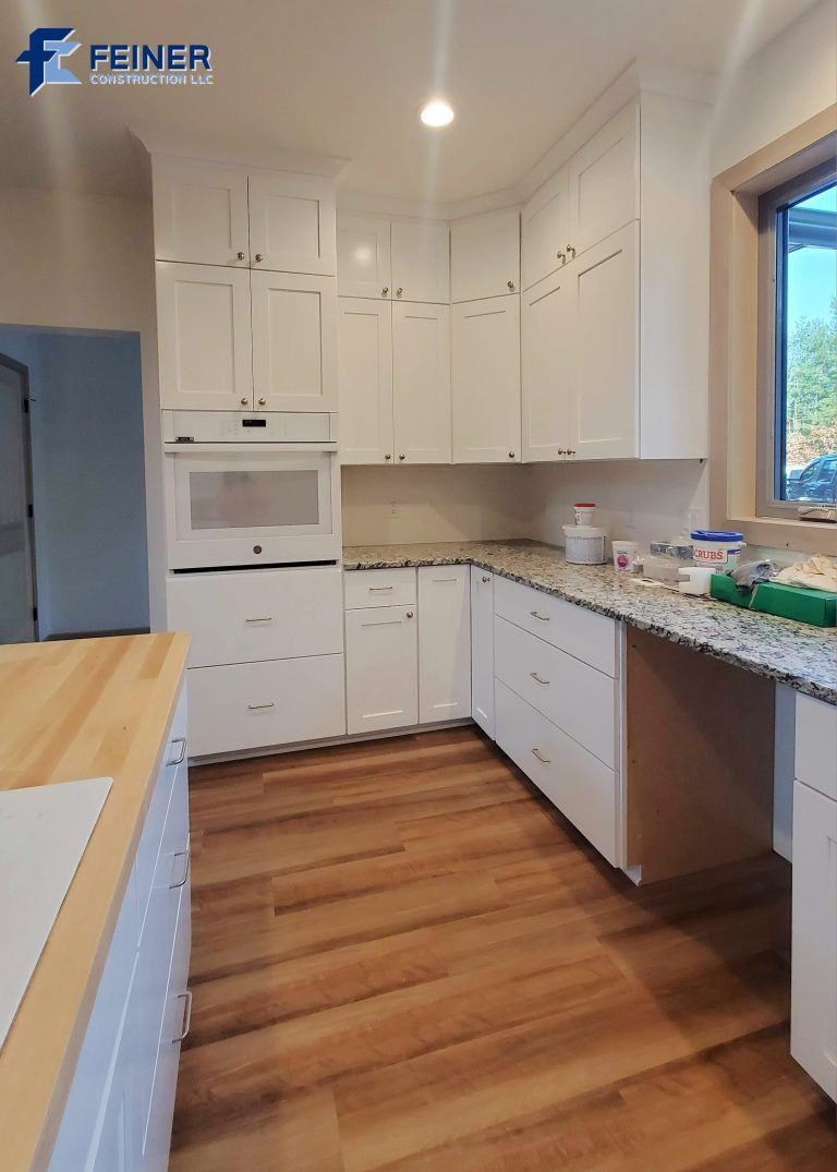 White kitchen with cabinets, built-in oven, granite countertops, and wood floors.