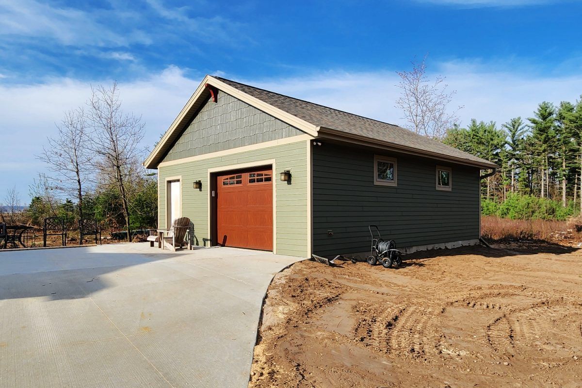 A green garage with a red garage door is sitting on top of a dirt hill.