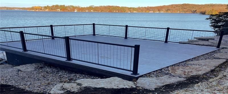 A deck overlooking a lake, surrounded by a black metal railing.