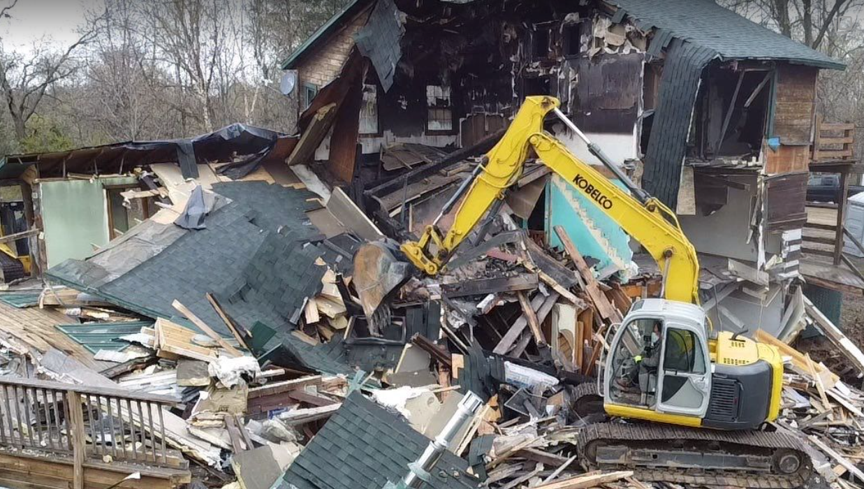 A yellow excavator is demolishing a house.
