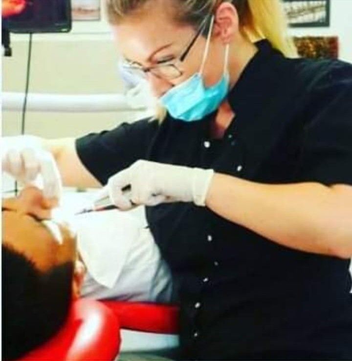 Dentista con mascarilla y guantes, examinando los dientes del paciente con herramientas dentales en la clínica.